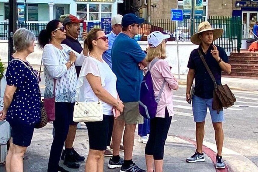 Un gruppo di persone in piedi su un marciapiede, alcune con cappelli e borse. 5