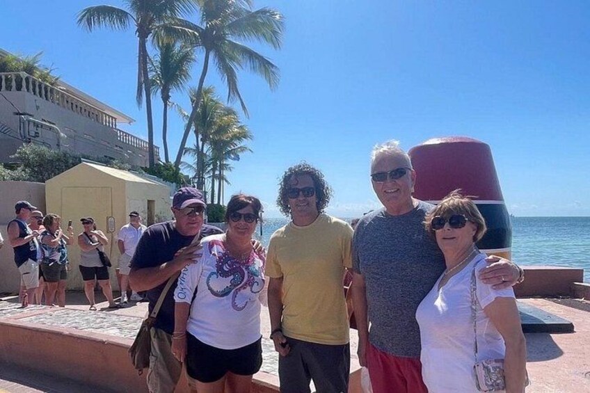 Un gruppo di persone in piedi su una spiaggia, con palme e un edificio sullo sfondo. 2