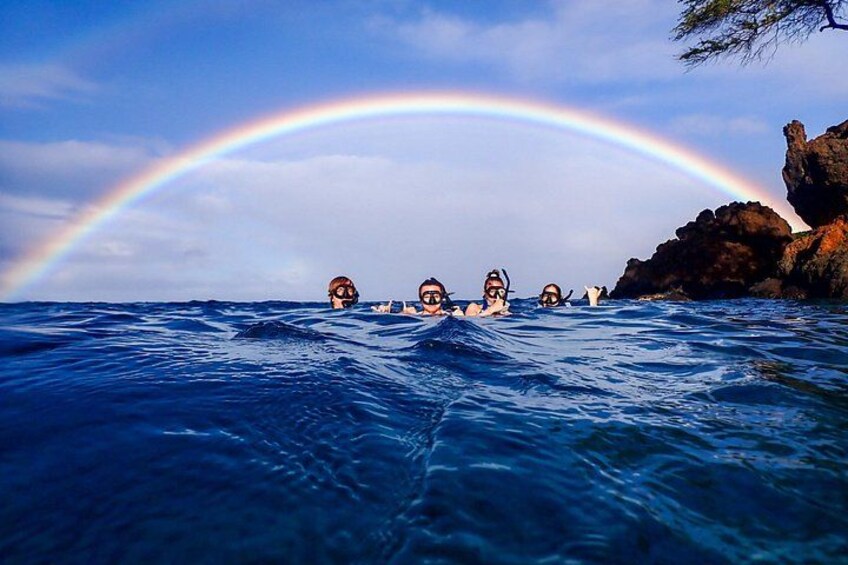 Een groep mensen snorkelt in de zee, met een regenboog op de achtergrond. 5