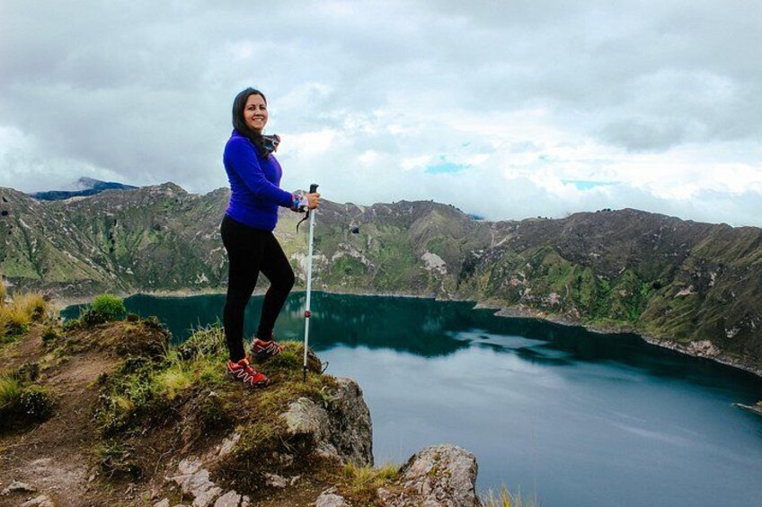 A person standing on a cliff with a hiking pole, overlooking a lake surrounded by mountains. 3