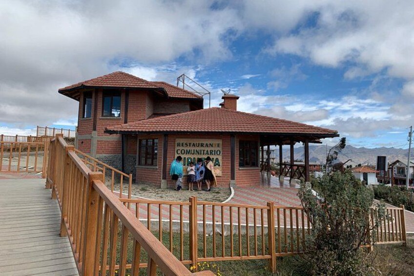 A brick building with a sign reading 'RESTAURANTE E COMUNITARIO,' a wooden deck, and a mountainous landscape in the background. 3