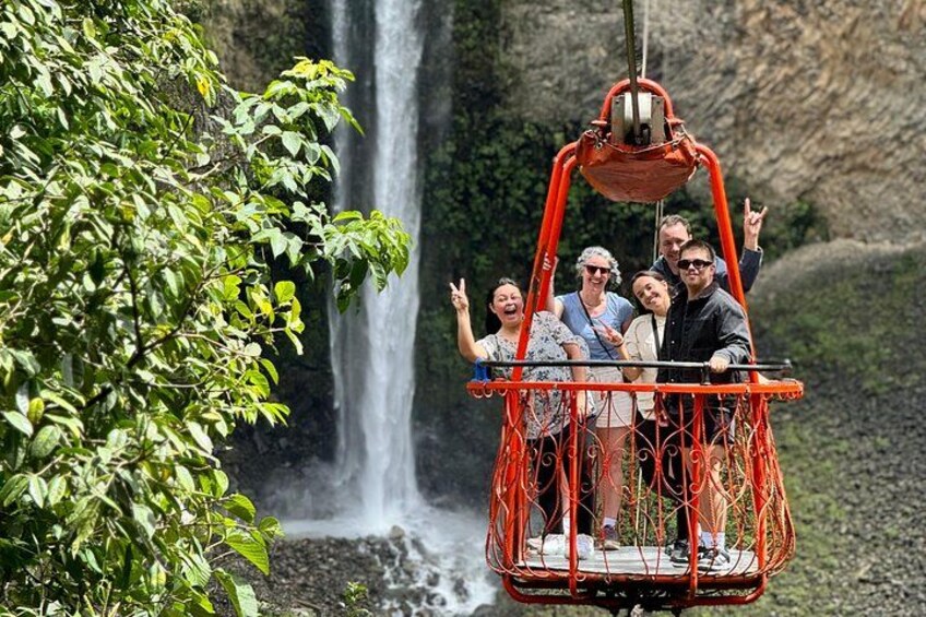 A group of people in a red cable car with a waterfall in the background. 4