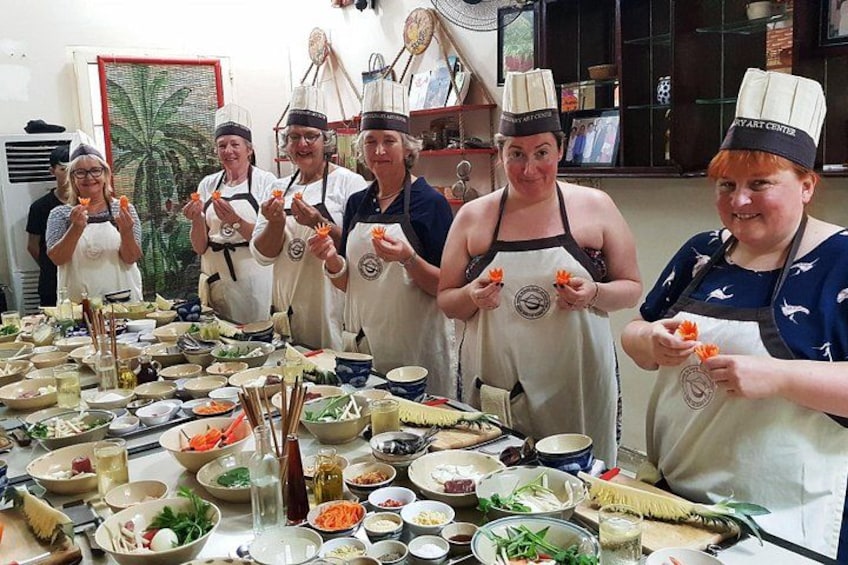 A group of people in aprons and chef hats, standing around a table with various cooking ingredients and utensils. 1