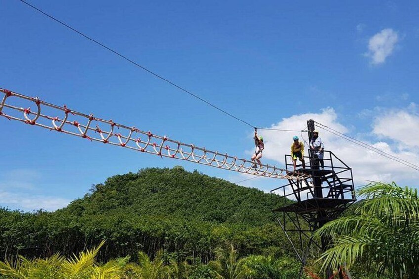 A zip line with people crossing over a forested hill. 2