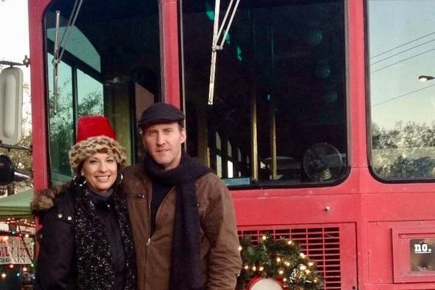 A red bus with a Christmas wreath and lights, a person wearing a hat, and another person in a jacket. 3
