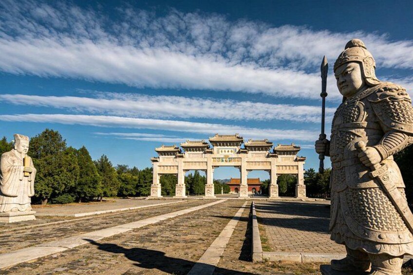 Een historisch bogenpoort met beelden en een stenen wachthoudende figuur. 1