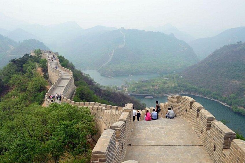 A stone wall with people walking along it, overlooking a river and mountains. 3
