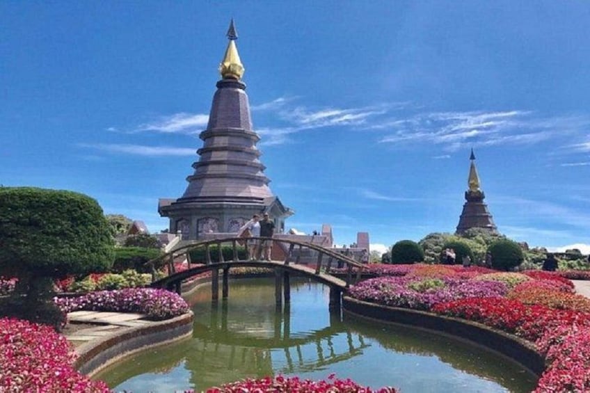 A temple with a golden spire, a bridge, and a pond surrounded by flowers. 2