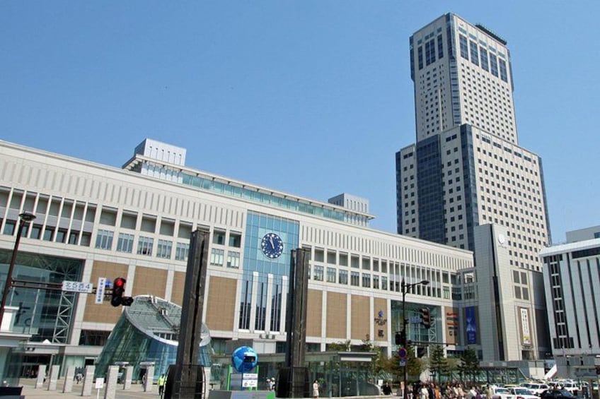 A modern building with a clock, a tall skyscraper, and a clear blue sky. 1