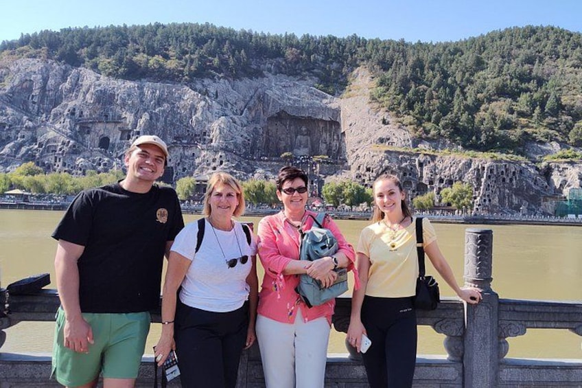 A group of people standing on a bridge with a rocky landscape and a river in the background. 1