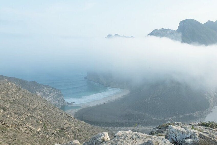 A coastal landscape with a rocky shoreline, a bay, and distant mountains partially obscured by fog. 5