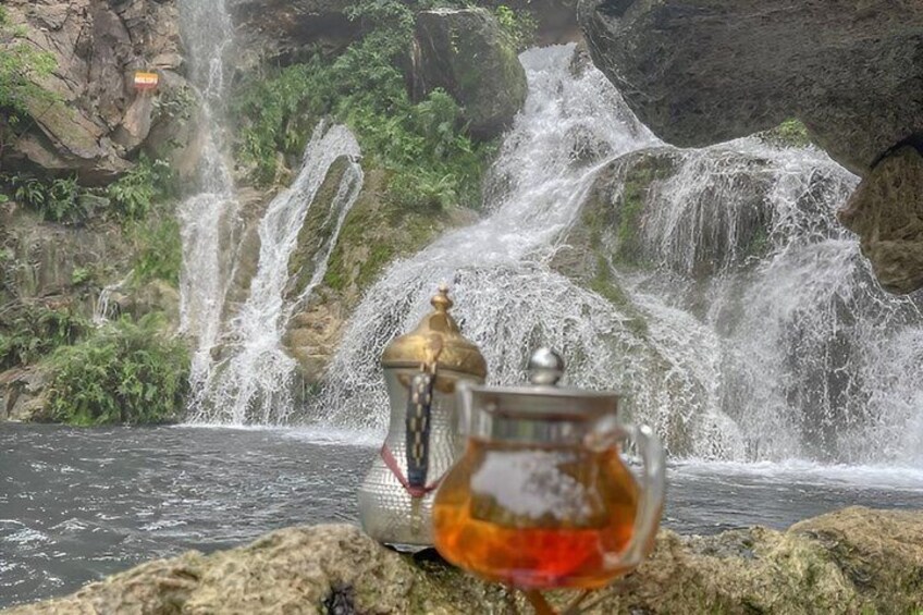 A waterfall, a glass teapot, and a metal teapot on a rock. 3