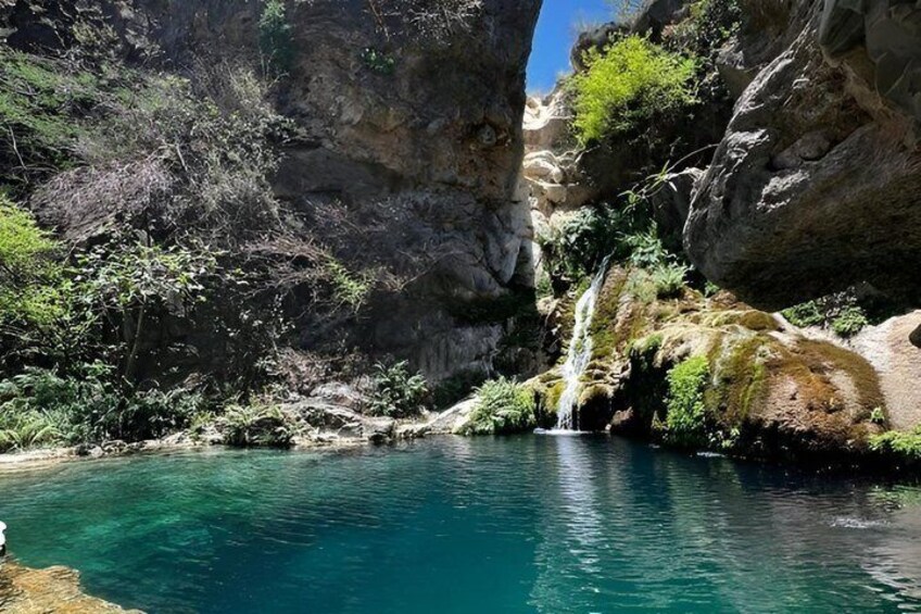 A turquoise pool surrounded by rocky cliffs and a waterfall. 5