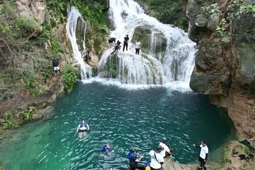 A waterfall cascading into a clear pool surrounded by rocky terrain. 1