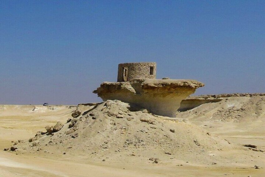 Paisaje desértico con una gran formación rocosa y una estructura pequeña en la cima. 2