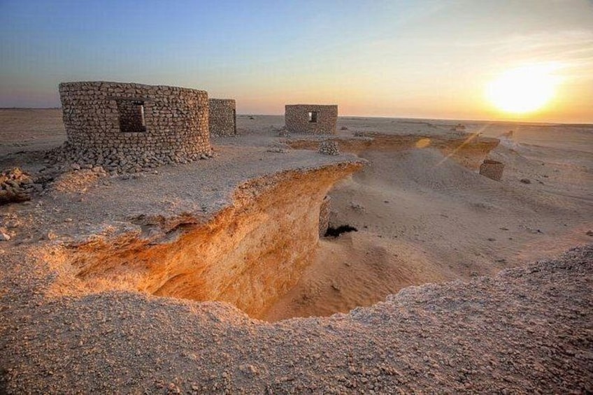 A desert landscape with a large sinkhole, stone structures, and a sunset. 2