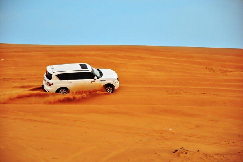 En vit SUV kör genom en öken med orangefärgade sanddyner. 2