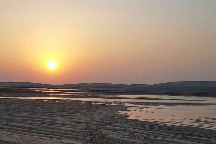 Ein Sonnenuntergang über einer ebenen Wüstenlandschaft, wobei sich ein Gewässer in der Sonne spiegelt. 2