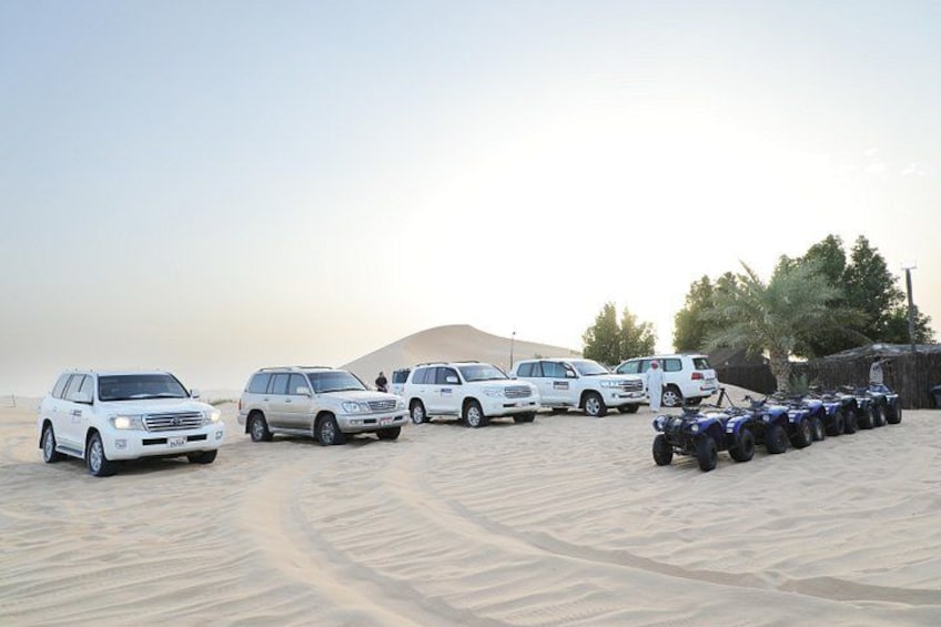 A desert landscape with several white SUVs and ATVs parked on the sand. 1