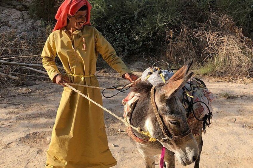 A person in a yellow robe leading a donkey with a saddle. 2