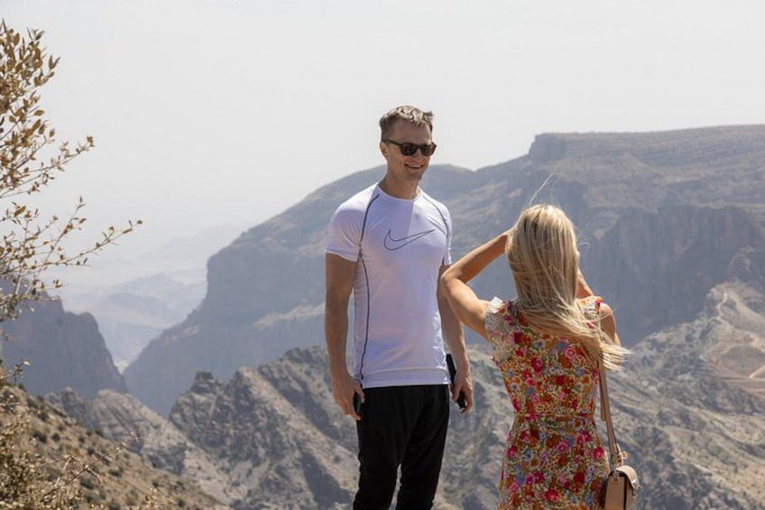 A couple standing on a mountain overlooking a canyon with rocky terrain and sparse vegetation. 2