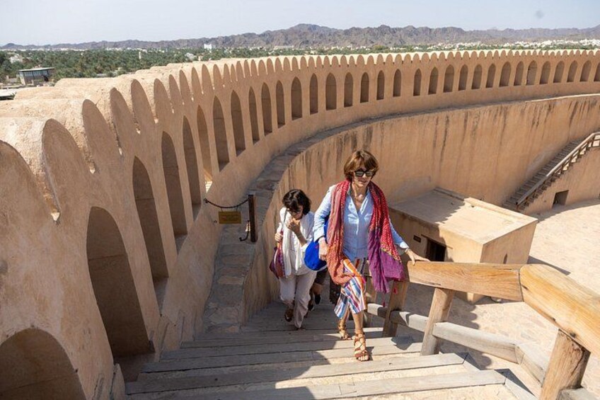 Una estructura de piedra curvada con arcos, escaleras de madera y un paisaje distante. 3