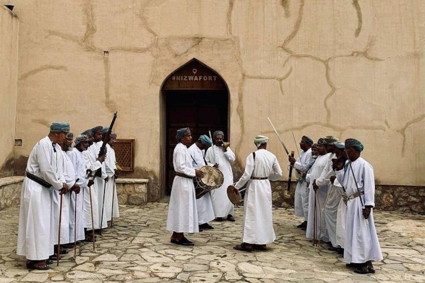 A group of men in white robes standing in front of a building with a sign that reads 'NIZWAFT.' 2