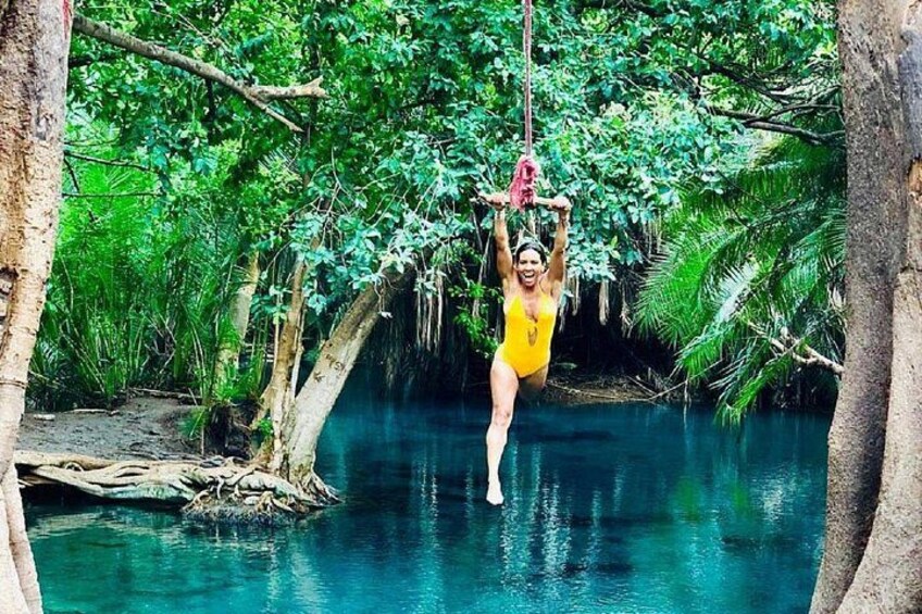 A person in a yellow swimsuit hanging from a rope in a forested area with a river. 4