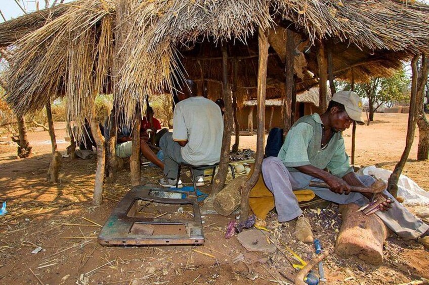 A rural setting with a thatched-roof hut, a man working with tools, and another person sitting nearby. 4