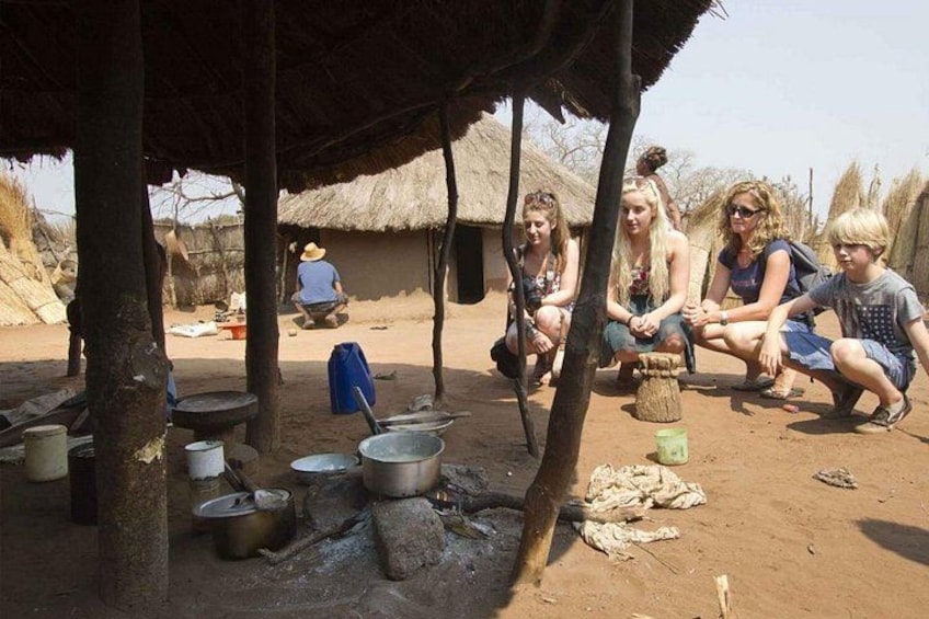 A group of people sitting under a thatched roof, cooking outdoors with pots and pans. 3