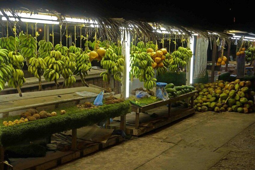 En nattmarknad med upphängda klasar av bananer och annan frukt. 4
