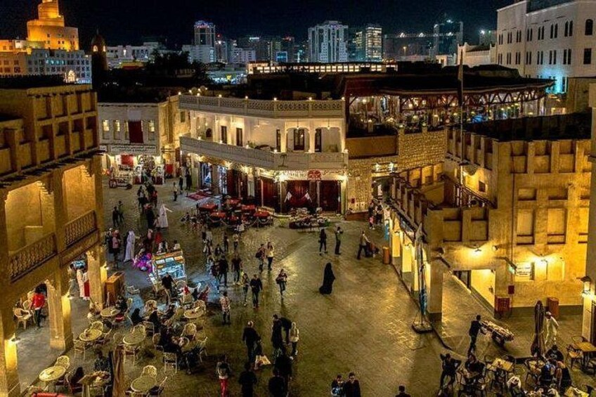 A bustling square with people, tables, and buildings at night. 1