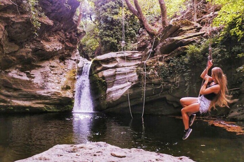 A woman swinging on a rope over a waterfall in a forested area. 1