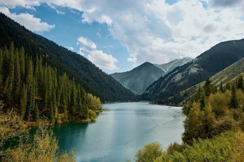 A calm lake surrounded by dense forests and mountains under a partly cloudy sky. 1