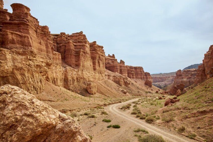 A canyon with a dirt road, red rock formations, and sparse vegetation. 2