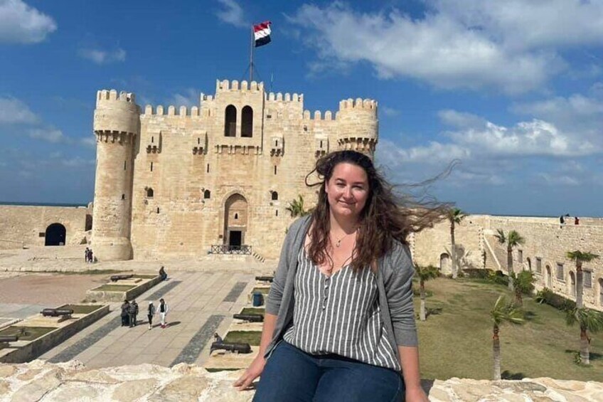 A woman sitting in front of a historic stone castle with a flag on top. 5