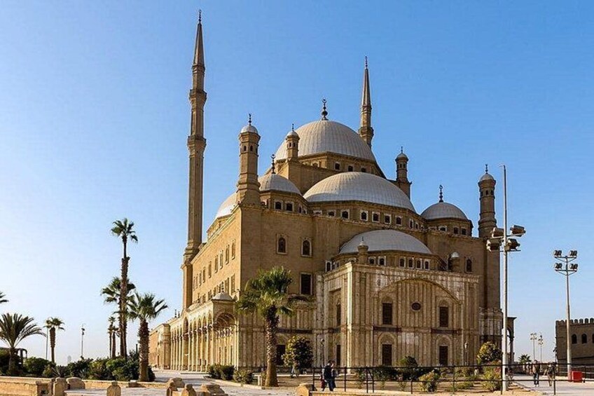 Una gran mezquita con numerosas cúpulas y minaretes, rodeada de palmeras y un cielo despejado. 2