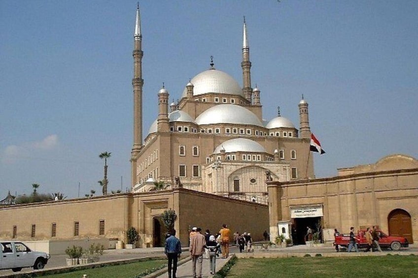 A large mosque with multiple domes and minarets, surrounded by a few people and vehicles. 2