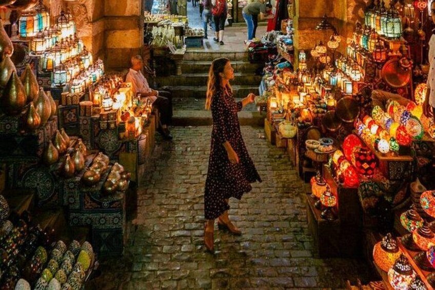 Una donna passeggia in un mercato con bancarelle che vendono ceramiche e lanterne. 2