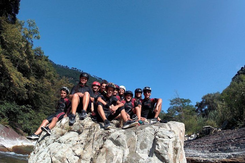 A group of cyclists resting on a rocky outcrop by a river. 1