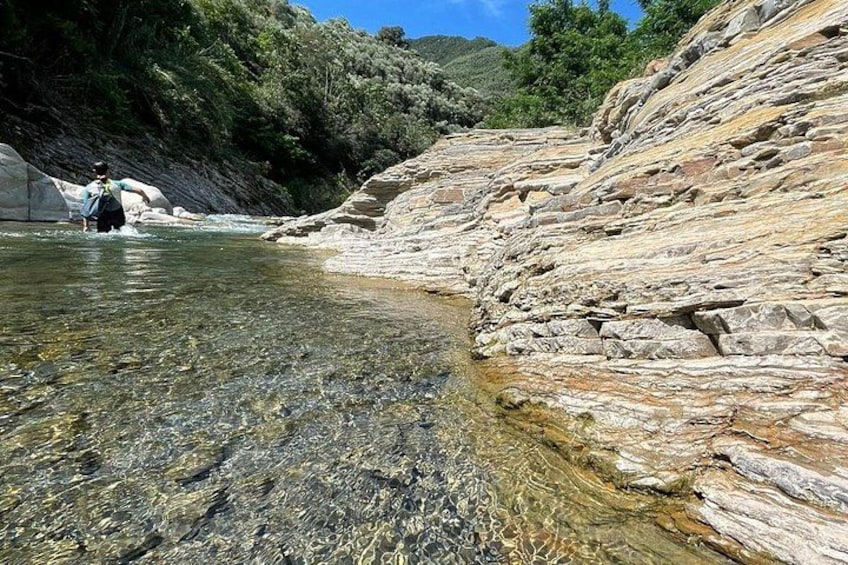 A clear river with rocks, a person wading, and a rocky hillside. 4