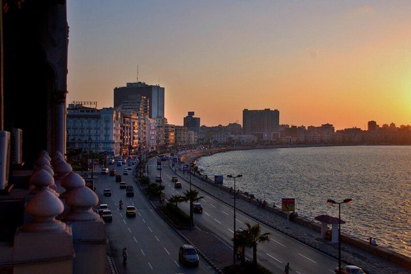 Un paisaje urbano costero al atardecer con una calle concurrida, edificios y un mar tranquilo. 1