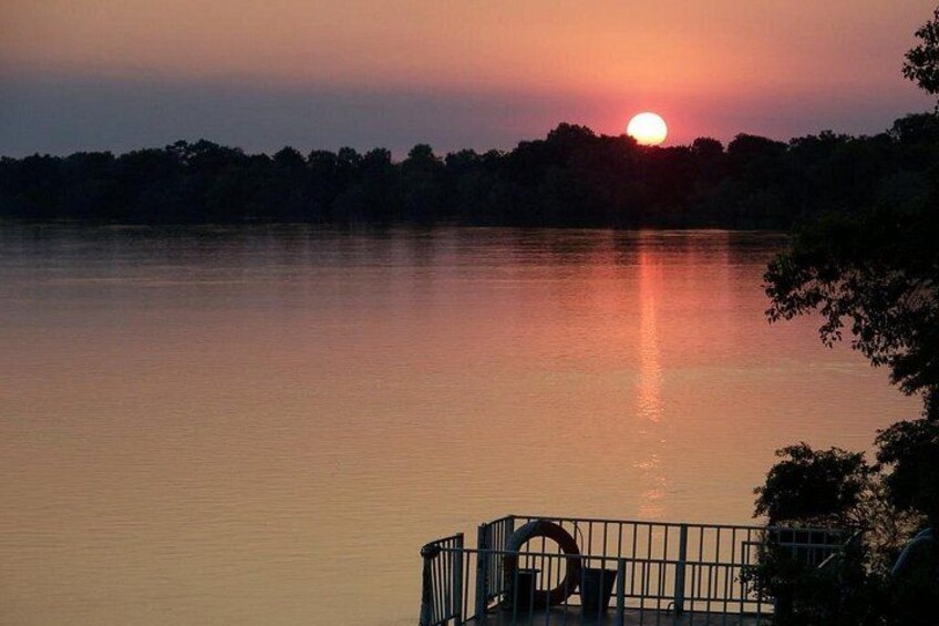 Un atardecer sobre un lago tranquilo con una valla y árboles en primer plano. 2