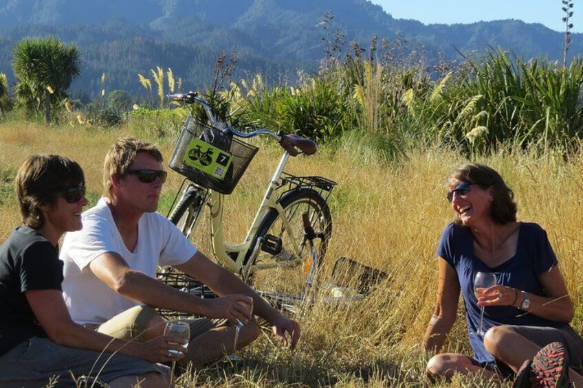 Tre personer sidder på græsset, med en cykel og en kurv i baggrunden. 2