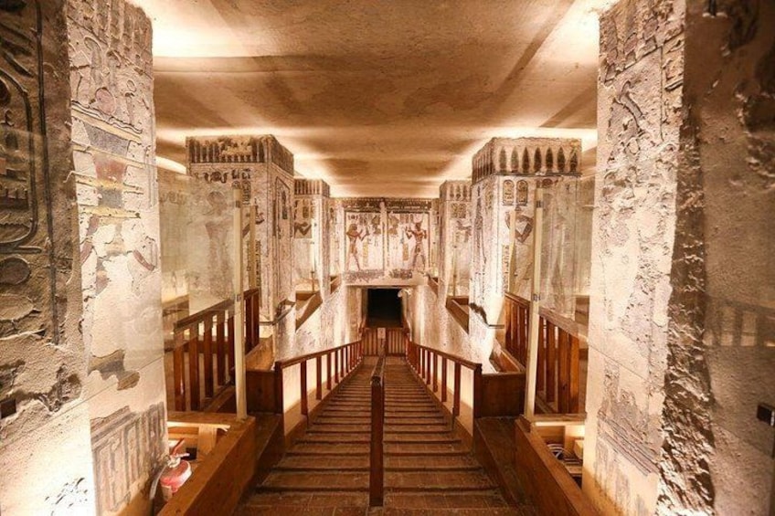 A corridor with hieroglyphs on the walls, wooden benches, and a staircase leading to a higher level. 5