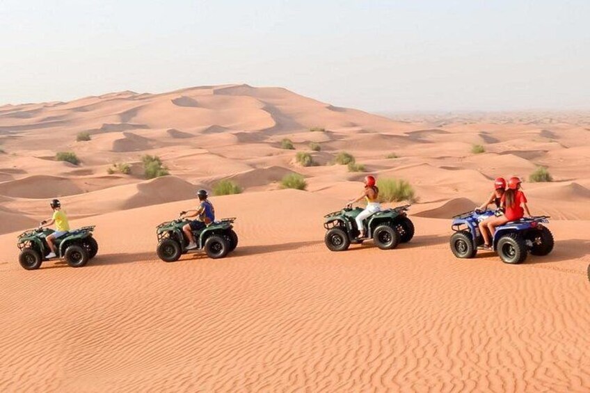 Quatre personnes sur des quads dans un désert, avec des dunes de sable en arrière-plan. 1