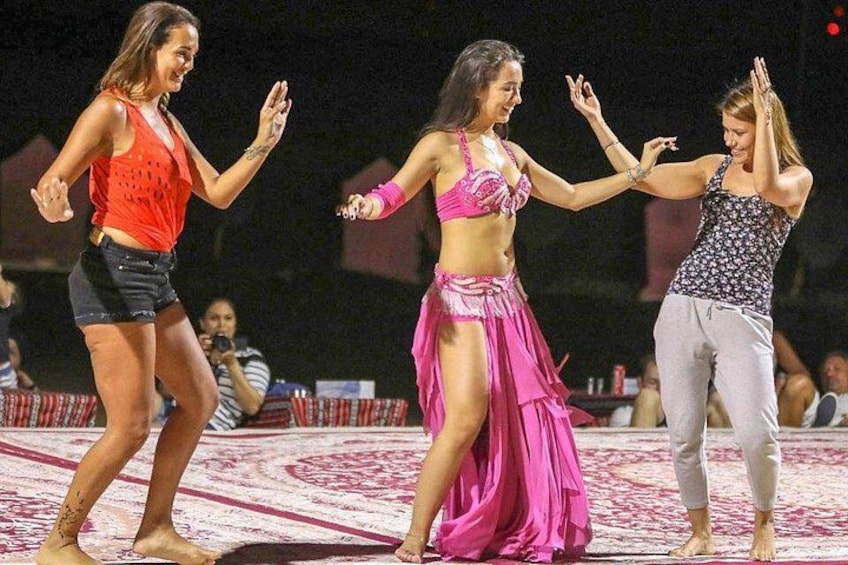 Drie vrouwen dansen op een podium met een patroonrijk tapijt. 2