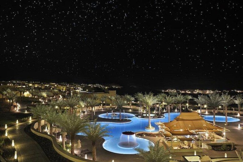 Un complexe hôtelier nocturne doté de piscines illuminées, de palmiers et d’un ciel étoilé. 5