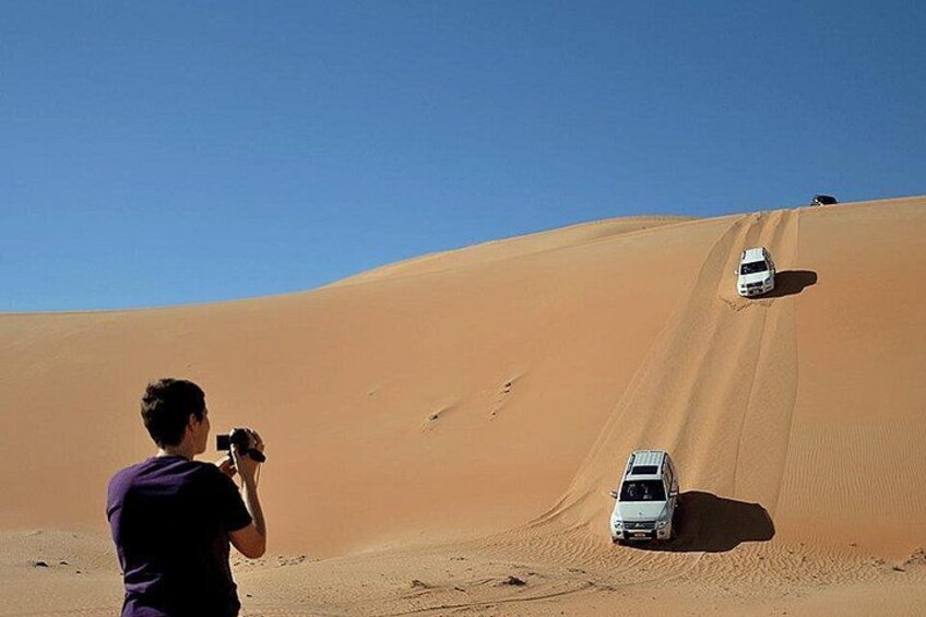 Une personne prend une photo d’un véhicule blanc descendant une dune de sable. 1