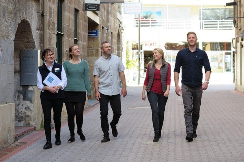 A group of people walking on a paved street with stone buildings and a signboard. 2
